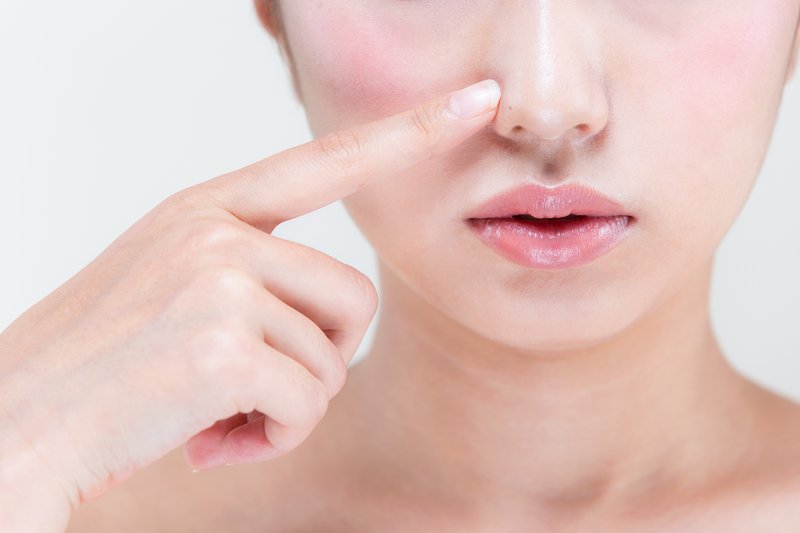 女性が頬のニキビを指で指しながら確認している