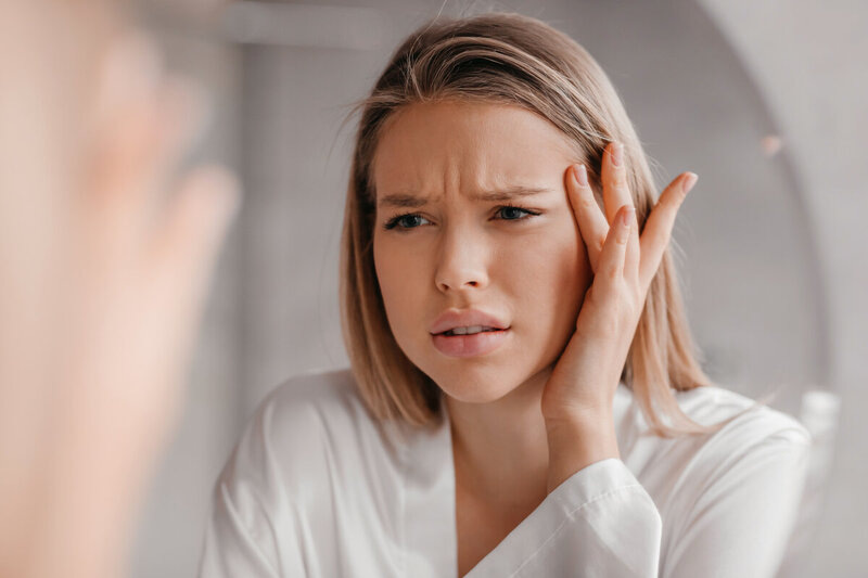 鼻の悩みを抱えた女性が思い詰めた表情でこめかみに手を当てている